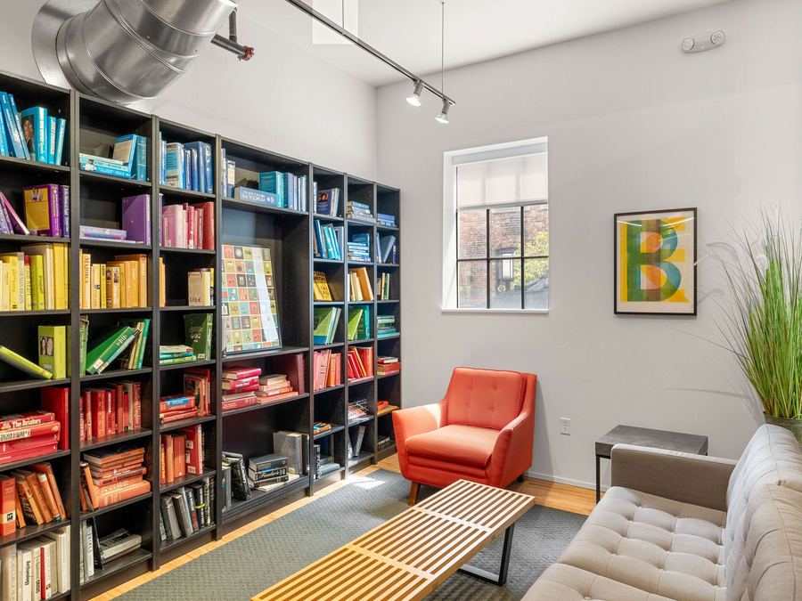 Reading lounge with floor-to-ceiling color-coded bookshelves and an orange armchair