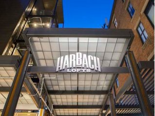 The dimensional Harbach Lofts sign lit up at dusk over the courtyard entrance